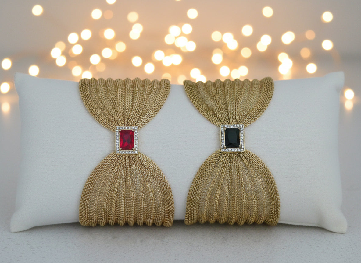 Pair of gold mesh earrings with gemstones on a white cushion.