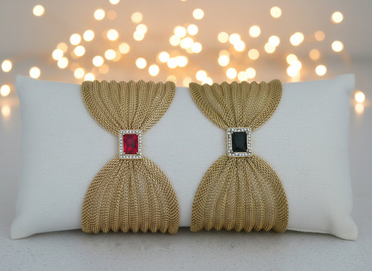 Pair of gold mesh earrings with gemstones on a white cushion.