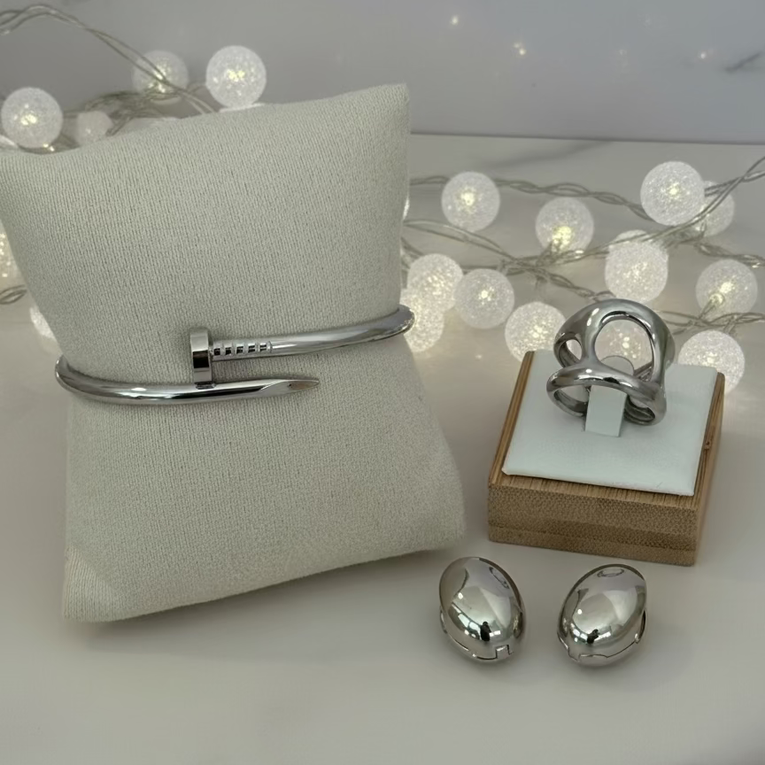 Silver bracelet, ring, and earrings on a marble surface with a neutral background